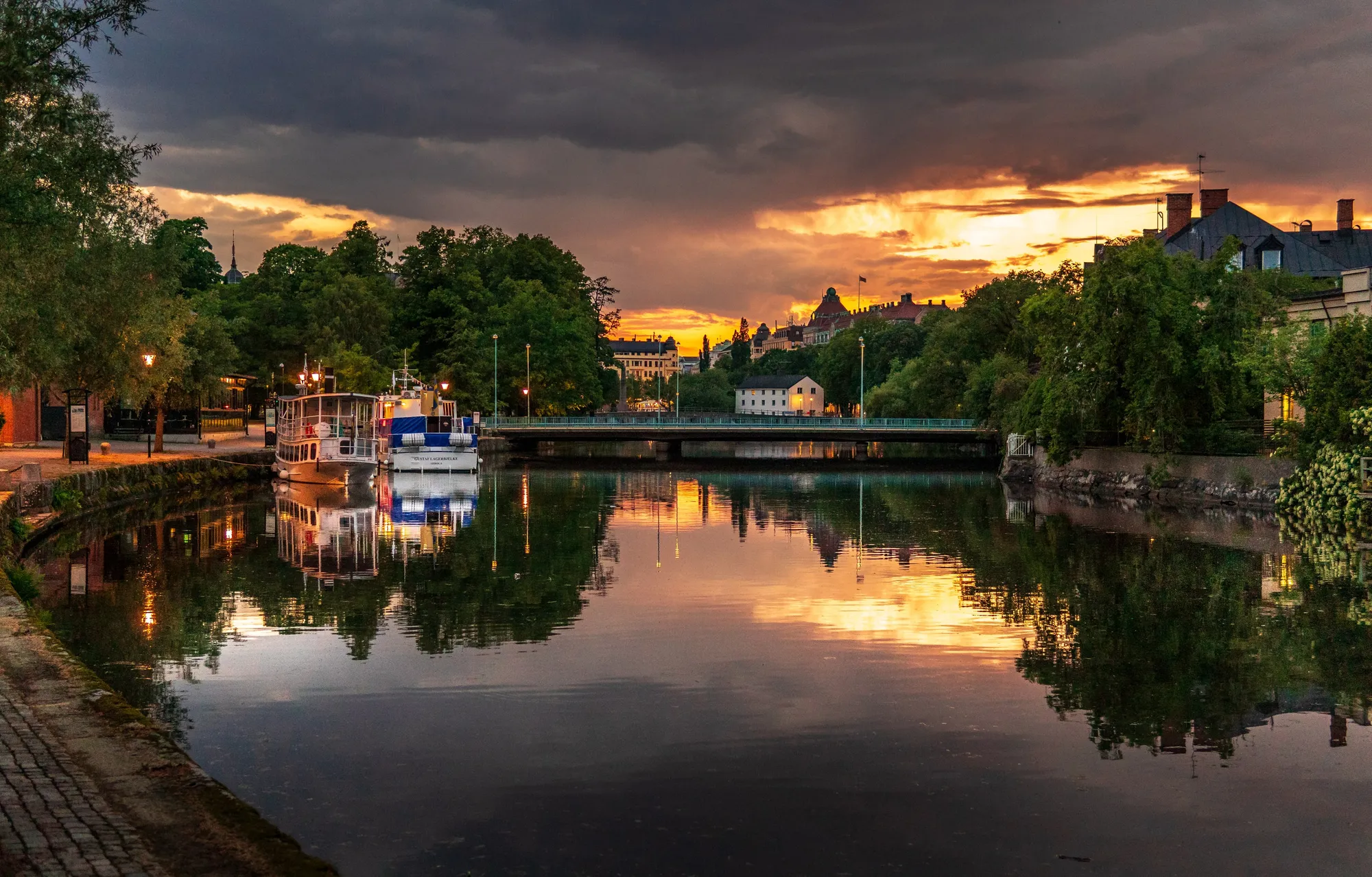 Kvällsljus över Svartån i Örebro, med båtar vid kajen och en bro i bakgrunden